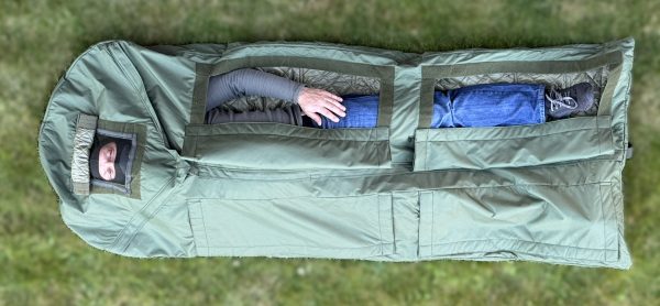 Person laying inside waterproof sleeping bag featuring hypothermia check openings for injury condition monitoring